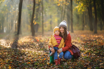 Pretty blonde little daughter with her mommy walks in autumn park - have funny and collect leaves