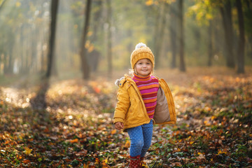 Cute baby girl in yellow coat and yellow knitted hat at autumn park.