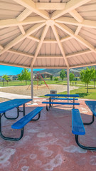 Vertical Blue picnic table and seats inside an octagon shape pavilion at a sunny park