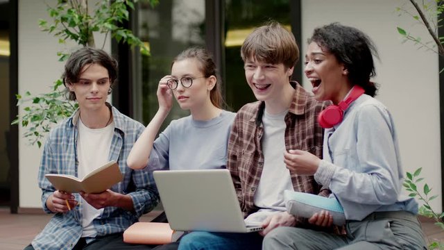 Medium shot of young emotional multinational students joyfully laughing studying together in university campus