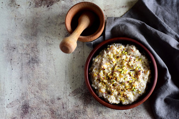 Delicious oatmeal porridge with crushed nuts in a clay plate, wooden mortar on a gray background