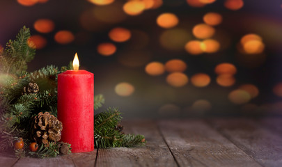 Candle and fir branches on wooden table. Background bokeh yellow lights