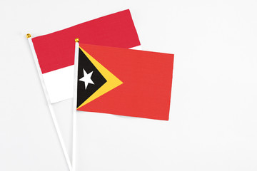 East Timor and Monaco stick flags on white background. High quality fabric, miniature national flag. Peaceful global concept.White floor for copy space.