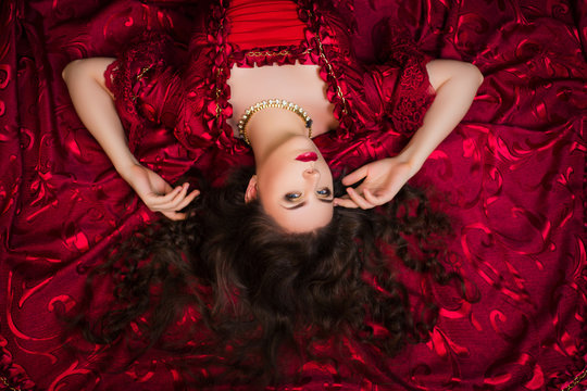 A beautiful young girl lies on a magnificent red dress of the Rococo era.