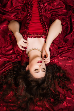 A beautiful young girl lies on a magnificent red dress of the Rococo era.