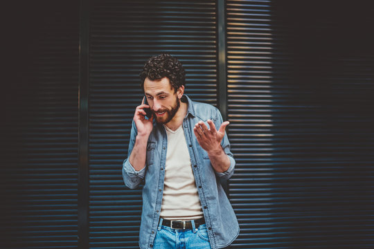 Annoyed bearded hipster guy dressed in casual wear calling on smartphone and solving conflict during phone conversation.Young man disagree with solution of problem talking on cellular
