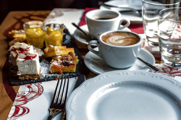 Dessert mix chocolate brownie cheese cream cake with peanuts and almonds sprinkled with powdered sugar two cups of coffee Americano and cappuccino.