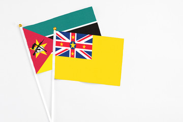 Fototapeta premium Niue and Mozambique stick flags on white background. High quality fabric, miniature national flag. Peaceful global concept.White floor for copy space.