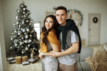 happy couple in love in the morning near the Christmas tree, a guy hugs a girl, morning Christmas. hearth, home clothes and sweaters.