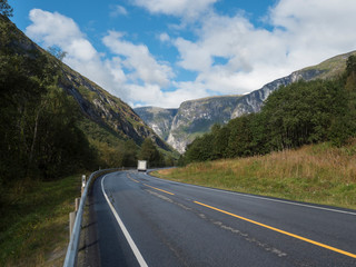White camper van car at Winding road E136 with mountain massif Trolltindene, Troll wall Trollveggen in Romsdal valley, Norway. Blue sky white clouds. Summer road trip travel scenery.