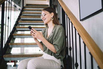 Fototapeta premium Satisfied female resting on stairs and messaging on cellphone