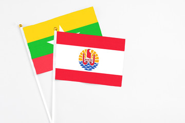 Fototapeta premium French Polynesia and Myanmar stick flags on white background. High quality fabric, miniature national flag. Peaceful global concept.White floor for copy space.