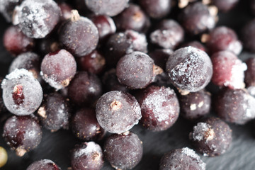natural frozen blackcurrant berries covered with hoarfrost scattered on a slate dish.