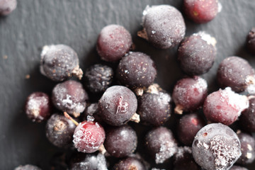 natural frozen blackcurrant berries covered with hoarfrost scattered on a slate dish.