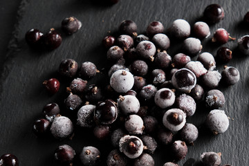 natural frozen blackcurrant berries covered with hoarfrost scattered on a slate dish.