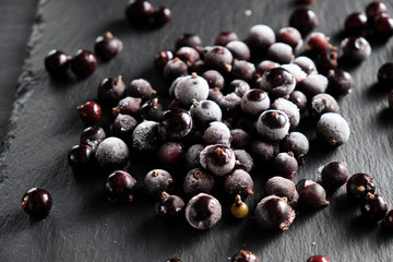 frozen blackcurrant berries covered with hoarfrost scattered on a slate dish.