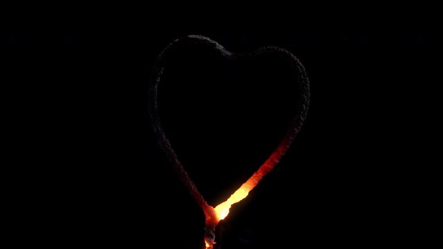 Celebrating love with a red hot glowing and burning heart shaped sparkler with golden sparks cascading against a black background.