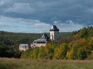 Karlstejn gothic state castle near Prague, the most famous castle in Czech Republic with grass meadow and autumn colored trees and forest. Blue sky clouds background. Located near Prague.