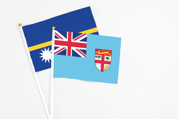 Fototapeta premium Fiji and Nauru stick flags on white background. High quality fabric, miniature national flag. Peaceful global concept.White floor for copy space.