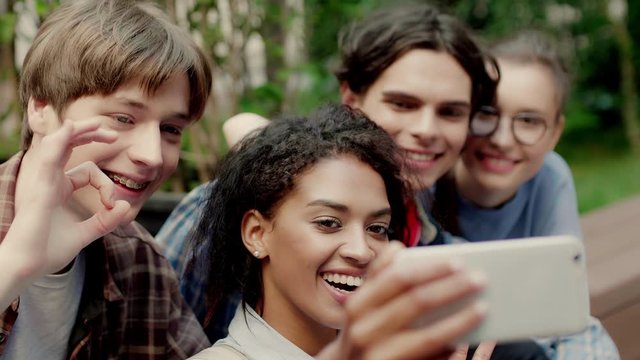 Close up shot of young casual multinational students happily taking selfie showing different gestures in university campus outdoor