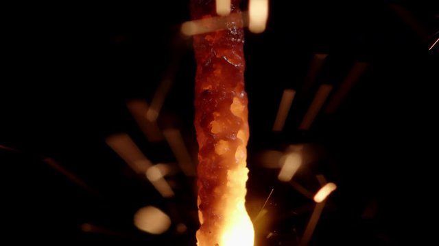 Macro shot of a red hot burning festive sparkler releasing golden sparkles while melting a chemical mixture of binders and metal powder.