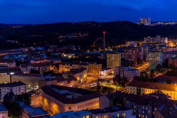 Crossing during late day to night timelapse to Mendel Square in Brno with cars and public transport, trams and buses passing through busy square and the surrounding streets which slowly light up.