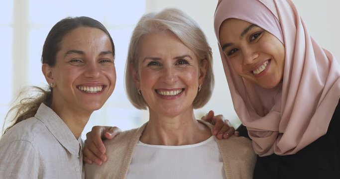 Three diverse smiling women friends embracing looking at camera