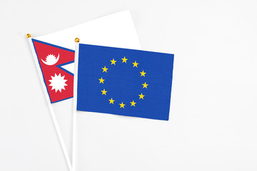 European Union and Nepal stick flags on white background. High quality fabric, miniature national flag. Peaceful global concept.White floor for copy space.