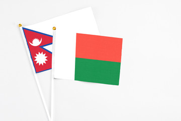 Madagascar and Nepal stick flags on white background. High quality fabric, miniature national flag. Peaceful global concept.White floor for copy space.