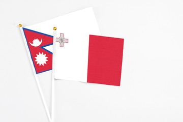 Malta and Nepal stick flags on white background. High quality fabric, miniature national flag. Peaceful global concept.White floor for copy space.