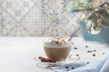 Cappuccino or latte in a glass cup on a light background. Female hand with a spoon
