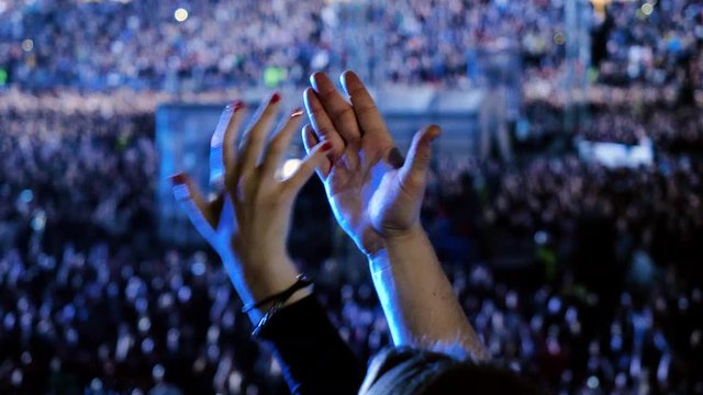 Music concert. A crowd of unrecognizable people applauding, dancing, jumping, raising their hands up, watching performance of a musical group on stage of music hall. 4K