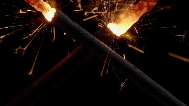 Two crossed ignited chrismas sparklers emitting golden sparks while the burning heat melts their metal together, forging them into a solid glowing cross.