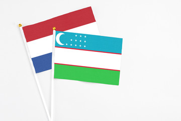 Uzbekistan and Netherlands stick flags on white background. High quality fabric, miniature national flag. Peaceful global concept.White floor for copy space.