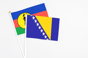 Bosnia Herzegovina and New Caledonia stick flags on white background. High quality fabric, miniature national flag. Peaceful global concept.White floor for copy space.