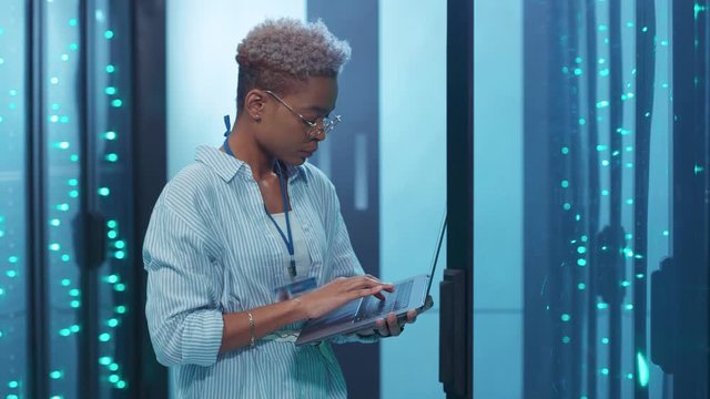 Professional african woman administrator running data center backups operation on open server rack cabinet working in digital high tech internet room.