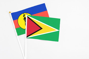 Guyana and New Caledonia stick flags on white background. High quality fabric, miniature national flag. Peaceful global concept.White floor for copy space.