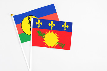 Guadeloupe and New Caledonia stick flags on white background. High quality fabric, miniature national flag. Peaceful global concept.White floor for copy space.