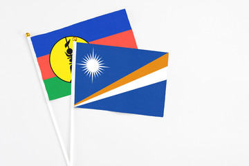 Marshall Islands and New Caledonia stick flags on white background. High quality fabric, miniature national flag. Peaceful global concept.White floor for copy space.