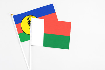 Madagascar and New Caledonia stick flags on white background. High quality fabric, miniature national flag. Peaceful global concept.White floor for copy space.