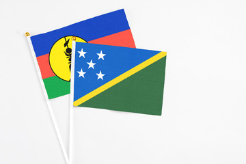 Solomon Islands and New Caledonia stick flags on white background. High quality fabric, miniature national flag. Peaceful global concept.White floor for copy space.