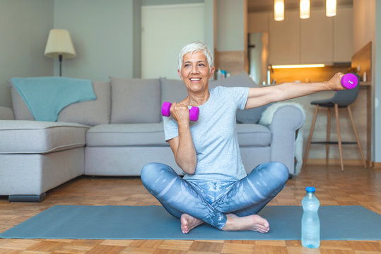 Portrait Of Senior Woman Exercising With Dumbbells At Home. Portrait Of An Older Woman In Sportswear Exercising With Dumbbells Indoors At Home. 