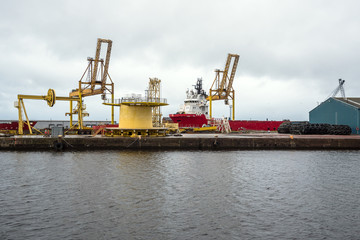 Fototapeta na wymiar Deep water port with quayside shipping cranes and a moored freight ship on a cloudy summer day. Leith, Edinburgh, Scotland