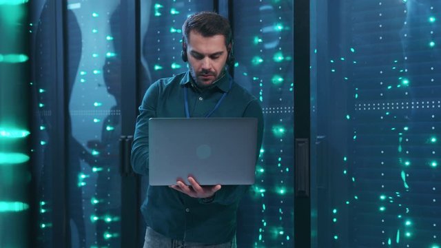 Server technician with laptop performing backups network operations with rack servers in digital high tech room webhosting working at data center.