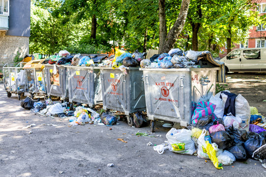 Rivne, Ukraine - July 4, 2018: Overflowing dirty dumpster with trash rubbish on the ground in Ukrainian city with cyrillic signs, plastic grocery bags