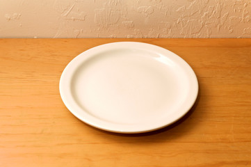 An old wooden counter against stuccoed wall with empty white ceramic plate or dish.