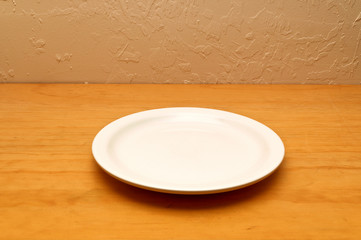 An old wooden counter against stuccoed wall with brightly lit empty white plate or dish.