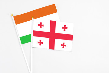 Georgia and Niger stick flags on white background. High quality fabric, miniature national flag. Peaceful global concept.White floor for copy space.