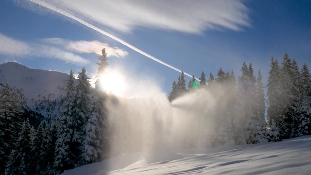 Schneekanone, Beschneinungslanze in Betrieb im Gegenlicht vor schneebedeckten B&auml;umen, blauen Himmel mit Wolken und Kondensstreifen