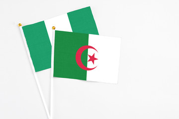 Fototapeta na wymiar Algeria and Nigeria stick flags on white background. High quality fabric, miniature national flag. Peaceful global concept.White floor for copy space.